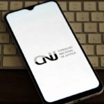 Smartphone exibindo o logo do CNJ em um teclado de computador
