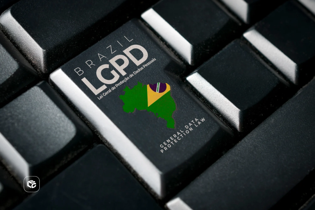Imagem em close de um teclado preto, com destaque para uma tecla personalizada contendo a inscrição “Brasil LGPD - Lei Geral de Proteção de Dados Pessoais”. Na mesma tecla aparece a silhueta do mapa do Brasil acompanhada de elementos nas cores da bandeira nacional e o texto em inglês “General Data Protection Law”. O restante do teclado permanece desfocado ao redor, reforçando o foco na tecla relacionada à proteção de dados. No canto inferior esquerdo há um pequeno logotipo branco. A composição remete à segurança digital, privacidade de informações e conformidade com a legislação brasileira de proteção de dados.