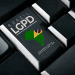 Imagem em close de um teclado preto, com destaque para uma tecla personalizada contendo a inscrição “Brasil LGPD - Lei Geral de Proteção de Dados Pessoais”. Na mesma tecla aparece a silhueta do mapa do Brasil acompanhada de elementos nas cores da bandeira nacional e o texto em inglês “General Data Protection Law”. O restante do teclado permanece desfocado ao redor, reforçando o foco na tecla relacionada à proteção de dados. No canto inferior esquerdo há um pequeno logotipo branco. A composição remete à segurança digital, privacidade de informações e conformidade com a legislação brasileira de proteção de dados.